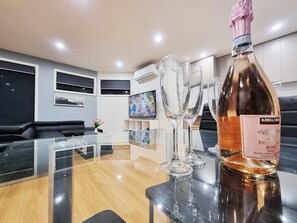 A modern living room with a glass table, a bottle of Kirkland Prosecco, and three wine glasses. - Rosie Townhouse - Modern and Comfortable Home (Sunshine North)