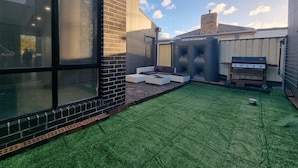 Ein moderner Hinterhof mit Kunstgrashalm, einem Grill und einer Sitzecke.