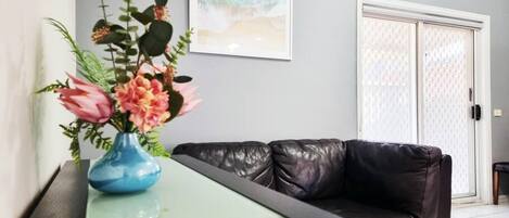 Una sala de estar moderna con una mesa de centro de vidrio, un sofá de cuero negro y un jarrón azul con flores.