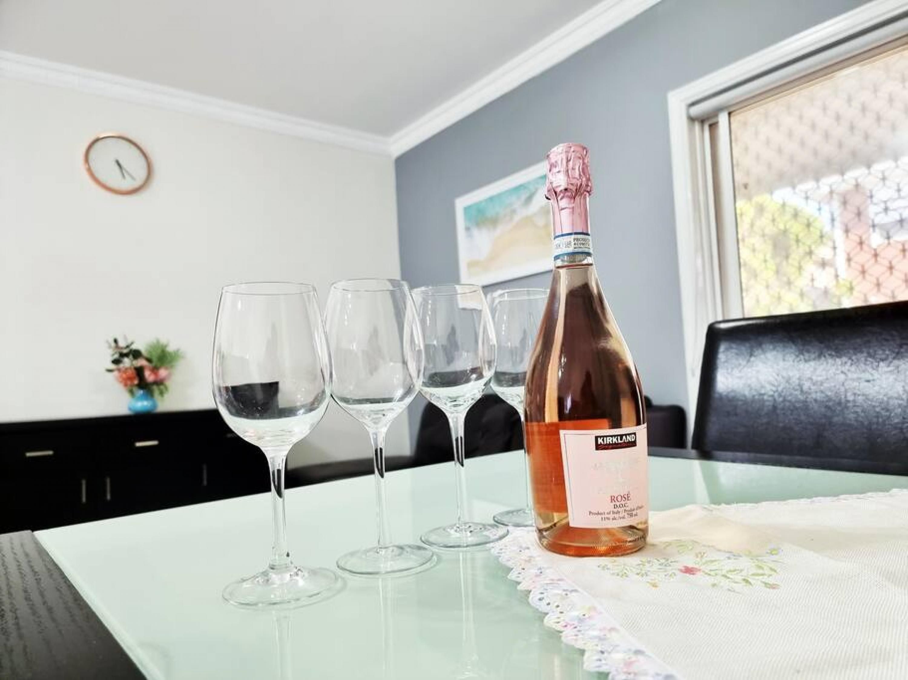 A table with a bottle of Kirkland Rose DOC wine and four empty wine glasses.