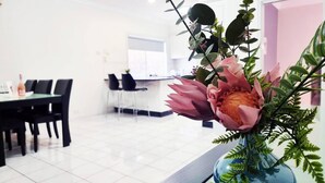 Ein moderner Essbereich mit Tisch und Stühlen, einer blauen Vase mit Blumen und einer Küche im Hintergrund.