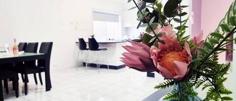 Ein moderner Essbereich mit Tisch und Stühlen, einer blauen Vase mit Blumen und einer Küche im Hintergrund.