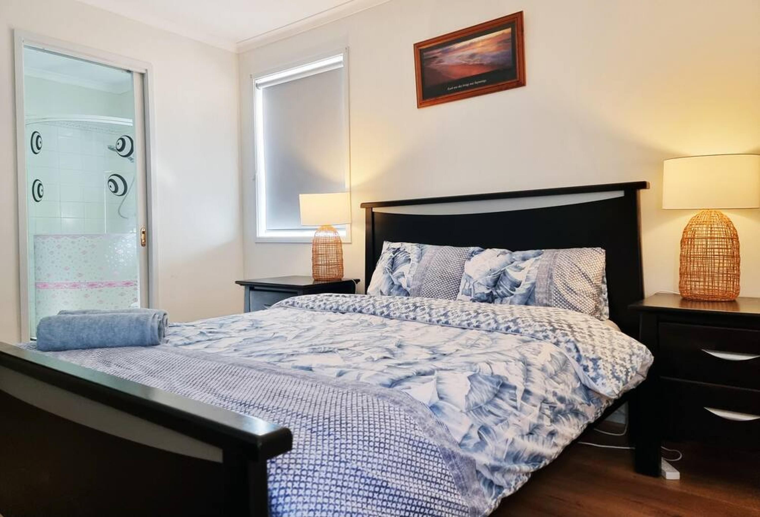 A bedroom with a bed, a window, a wall-mounted picture, and a bedside lamp.