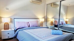 Ein modernes Schlafzimmer mit einem großen Bett, zwei Nachttischen, einem Spiegel und integrierten Klimaanlagen.
