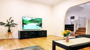 Ein modernes Wohnzimmer mit Flachbildfernseher, einer Ledersofa, einem Couchtisch und einer Treppe, die zu einer oberen Etage führt.