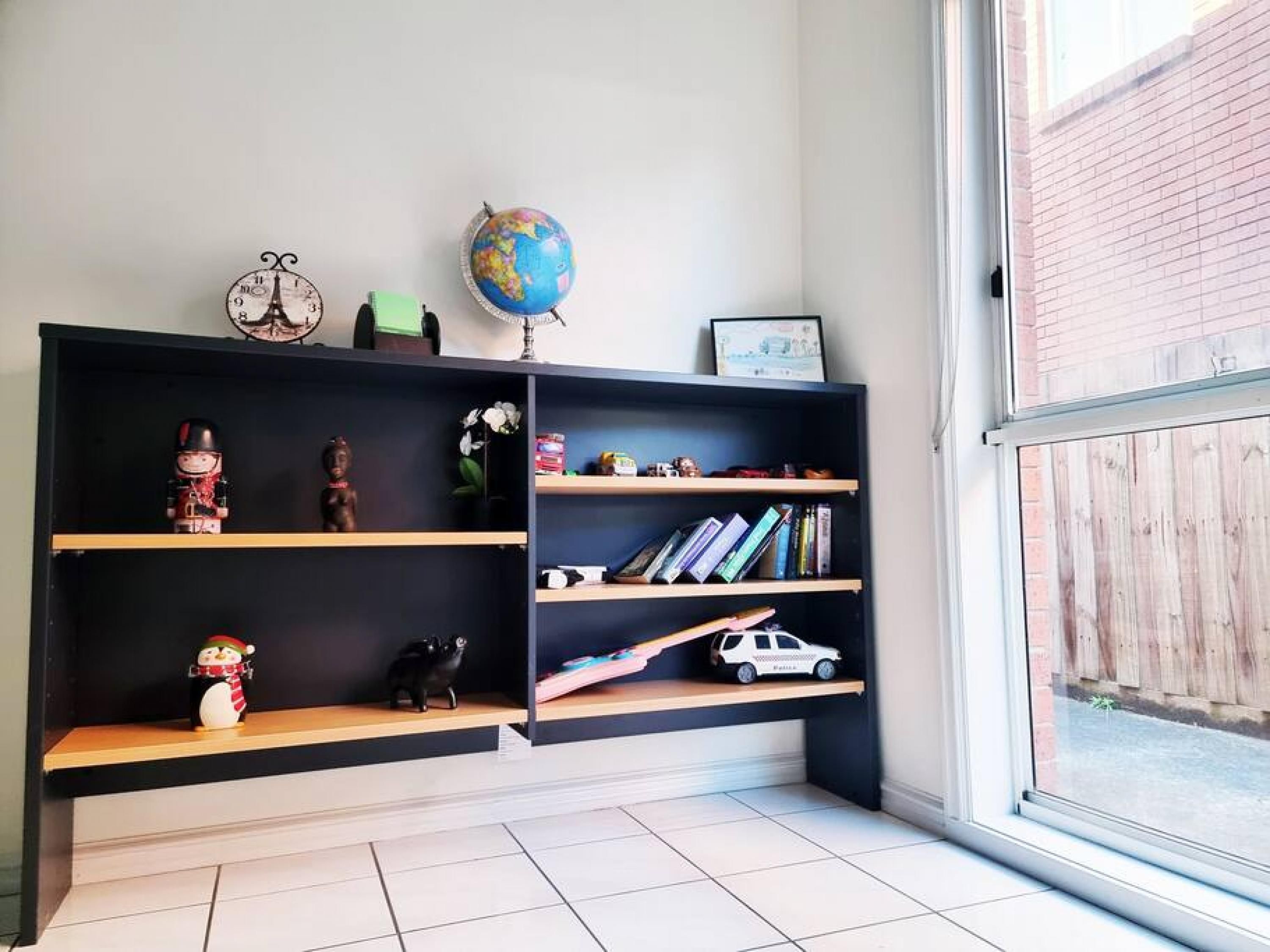 A modern living room with a black bookshelf, a globe, a clock, and a window with a view of a brick wall.