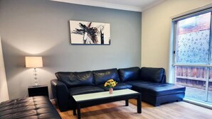 Ein modernes Wohnzimmer mit einem dunkelbraunen Ledersofa, dazu passend einem Ottomanen, einem Couchtisch mit Blumen in einer Vase und einem Gemälde an der Wand.