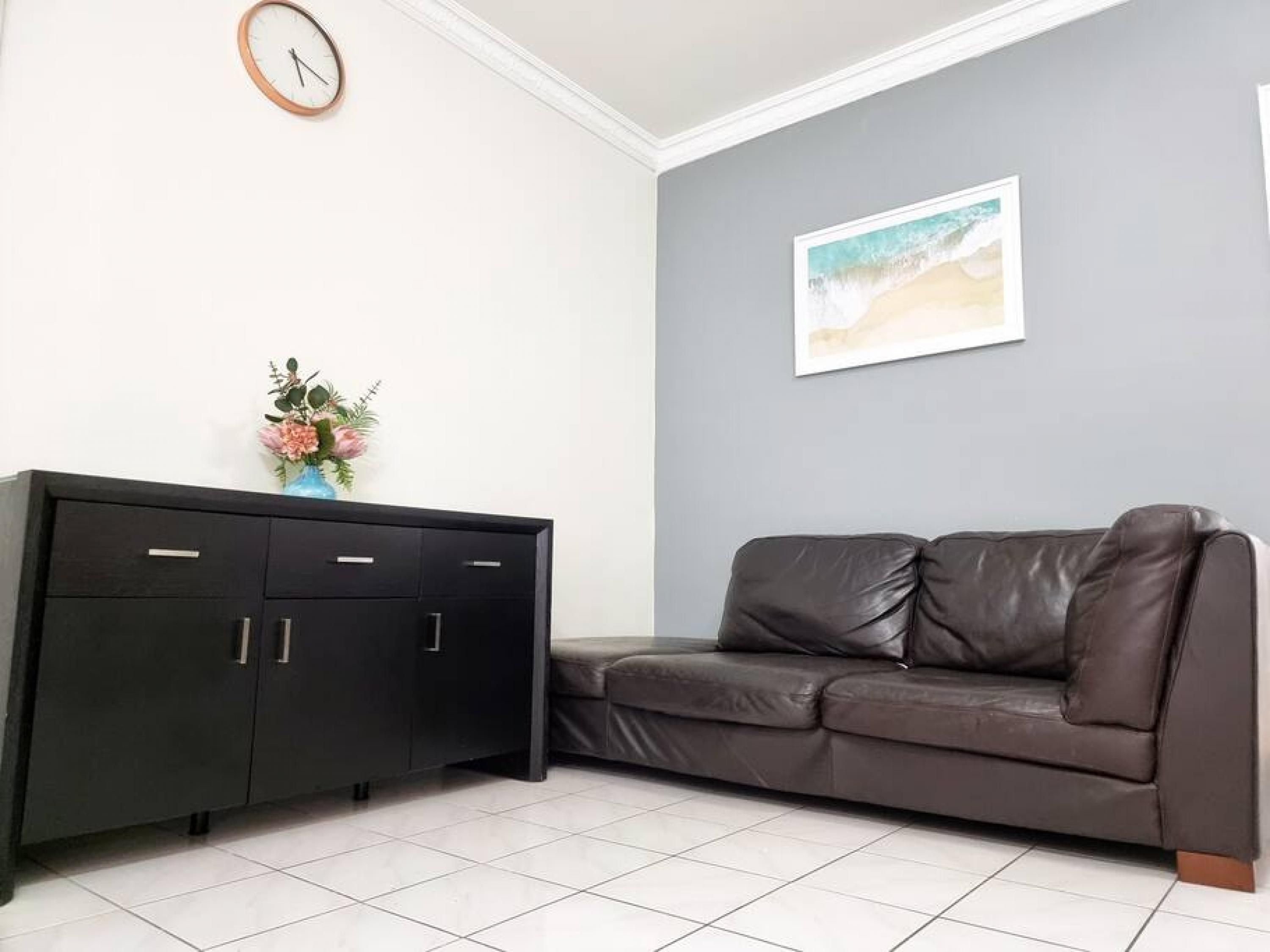 A living room with a dark brown leather sofa, a black cabinet, a clock, and a framed picture on the wall.