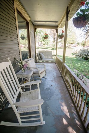 A porch with two rocking chairs and a small table, surrounded by a wooden railing. - Bridgewalk Estate a Wanderlust Abodes Property (Central Lake)