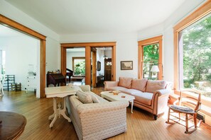 A spacious living room with a sofa, a coffee table, and a rocking chair. There is a piano in the background and a large window providing a view of the outdoors. - Bridgewalk Estate a Wanderlust Abodes Property (Central Lake)