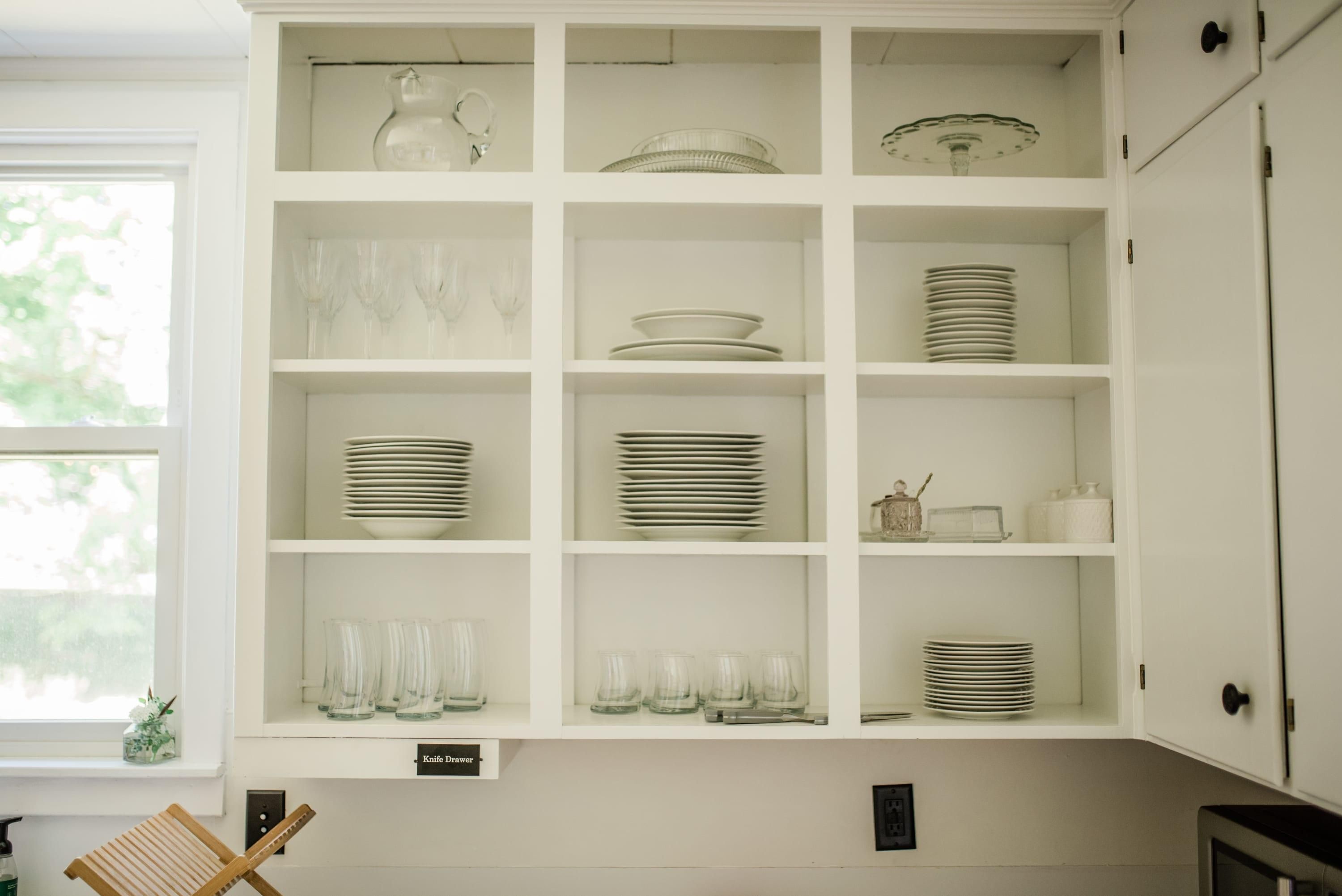 A kitchen with white cabinetry, glassware, and plates.