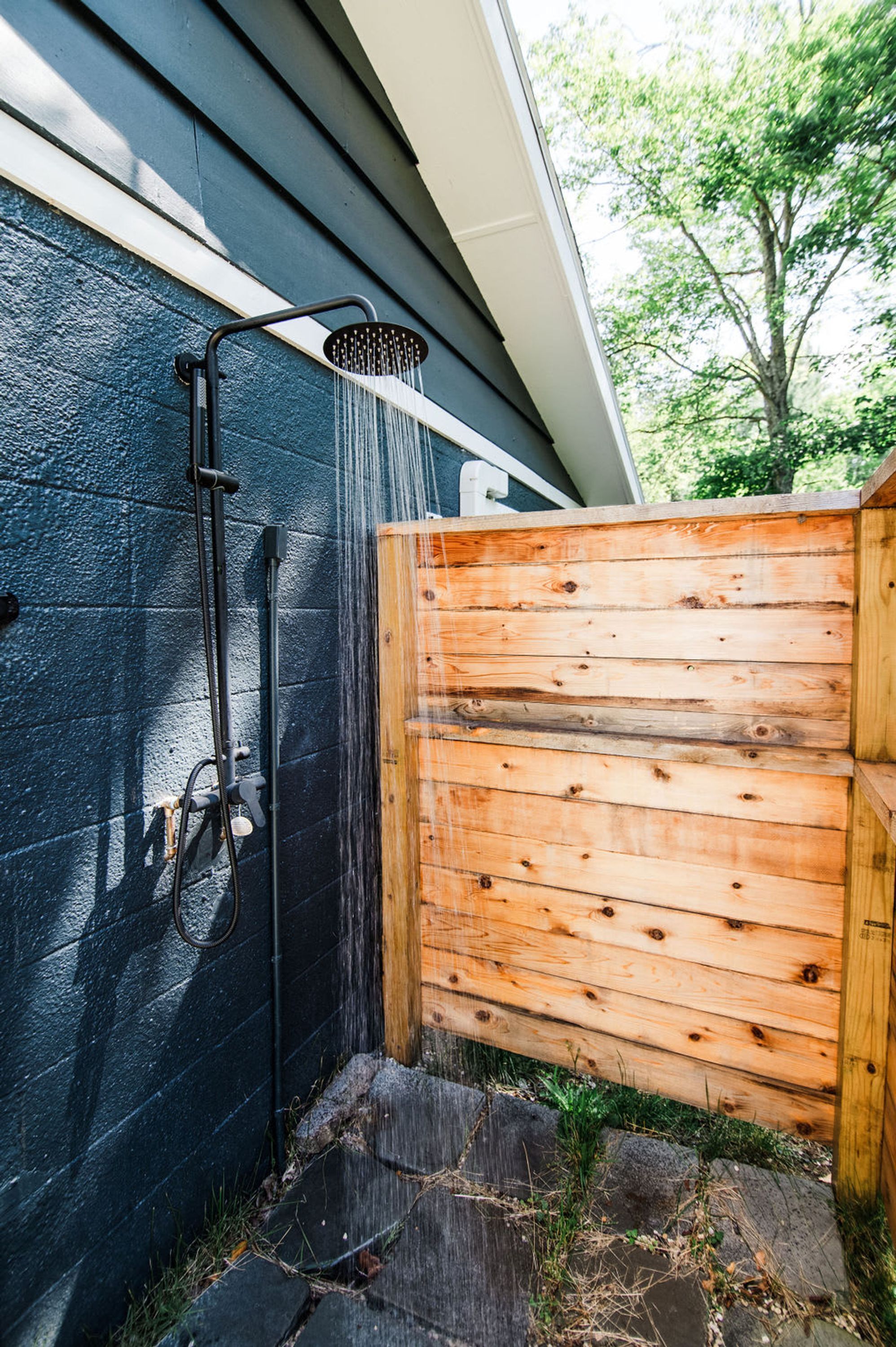 A wooden fence, a black wall, and a showerhead with water flowing.