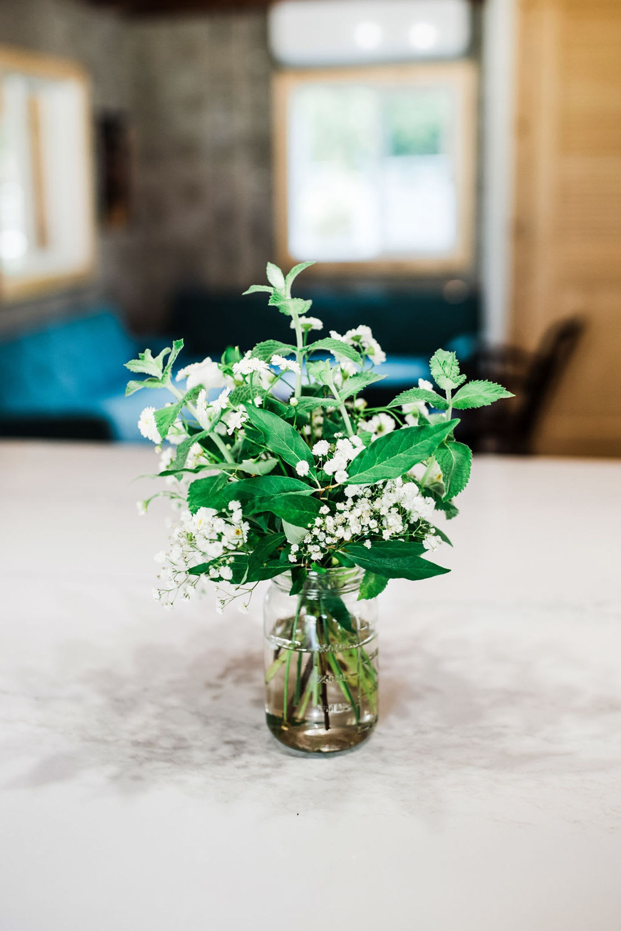 Een vaas met witte bloemen en groene bladeren op een marmeren tafel.