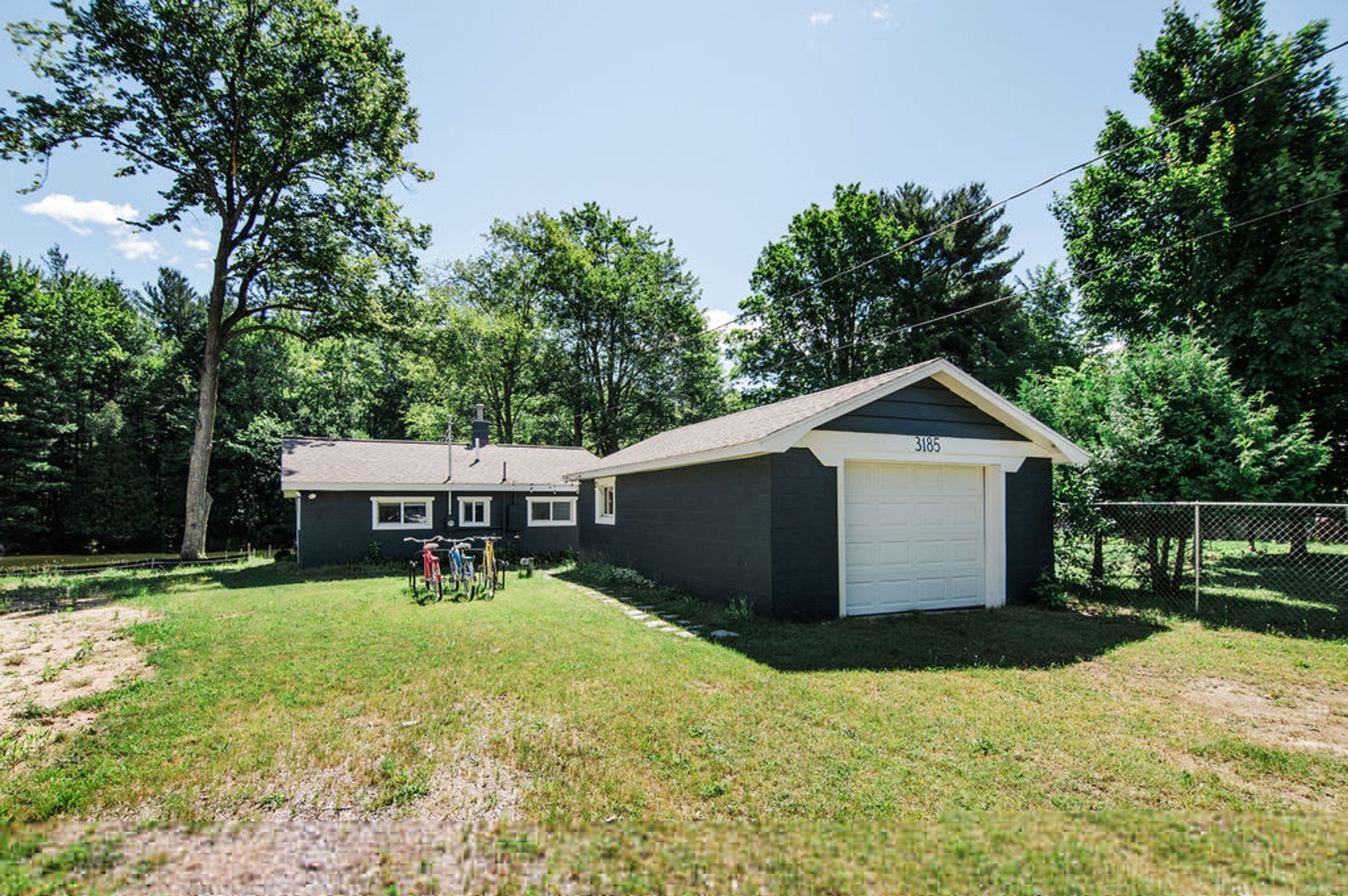 A single-story house with a garage, surrounded by a grassy yard and trees.