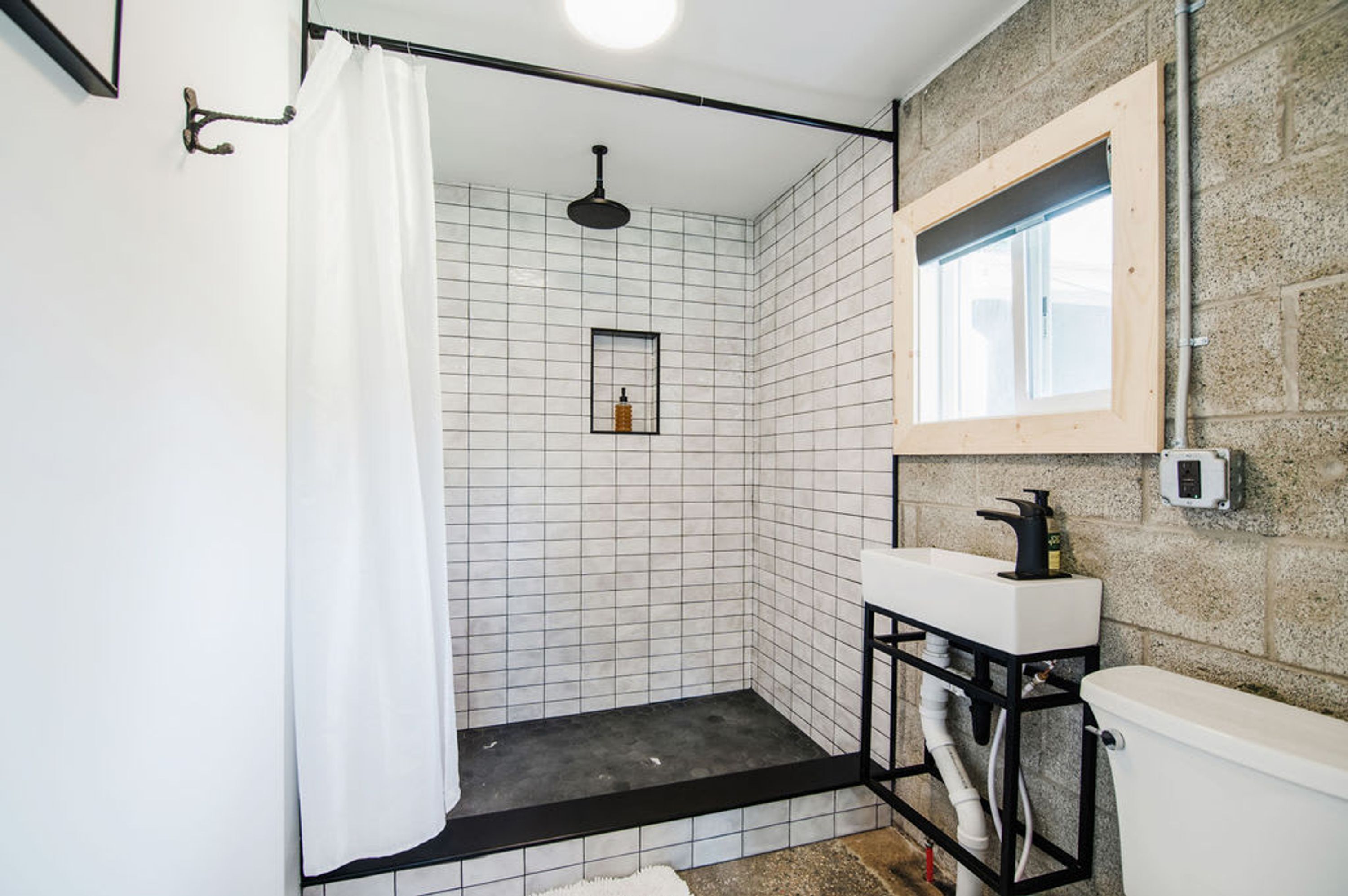 Een badkamer met een douche, toilet, wastafel en raam.
