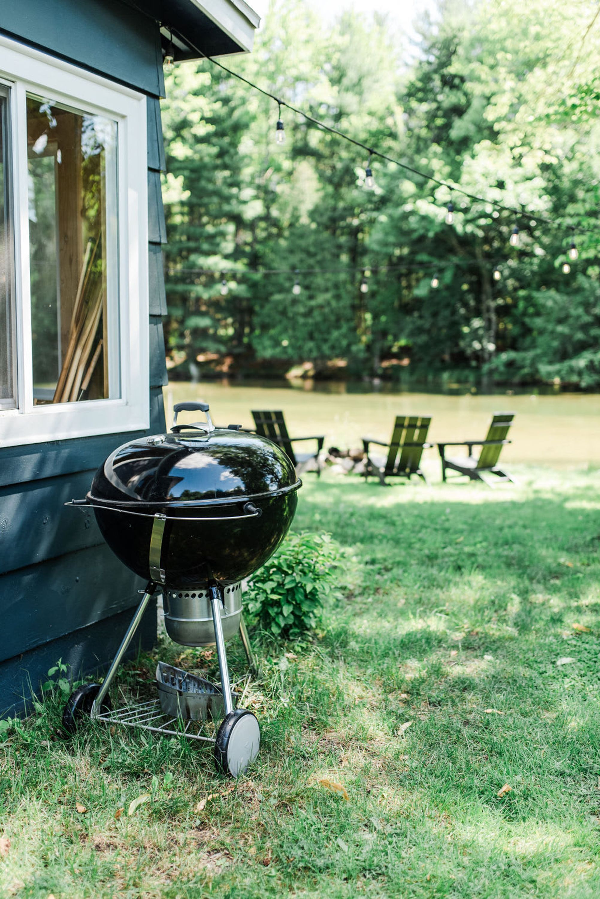 A barbecue grill outside a house with a grassy yard and a pond in the background.