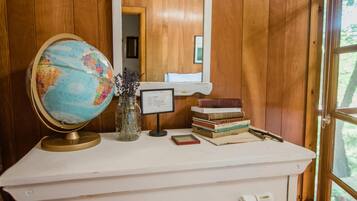 Une commode blanche avec des tiroirs, un globe terrestre, un vase avec des fleurs et une pile de livres, le tout placé contre un mur en bois avec un miroir au-dessus.