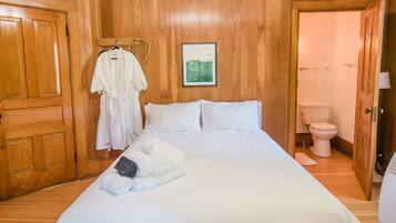 A bedroom with wooden paneling, a bed with white linens, a hanging robe, and a framed picture on the wall.