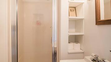 Un baño con ducha de vidrio, un lavamanos blanco y un espejo en la pared.