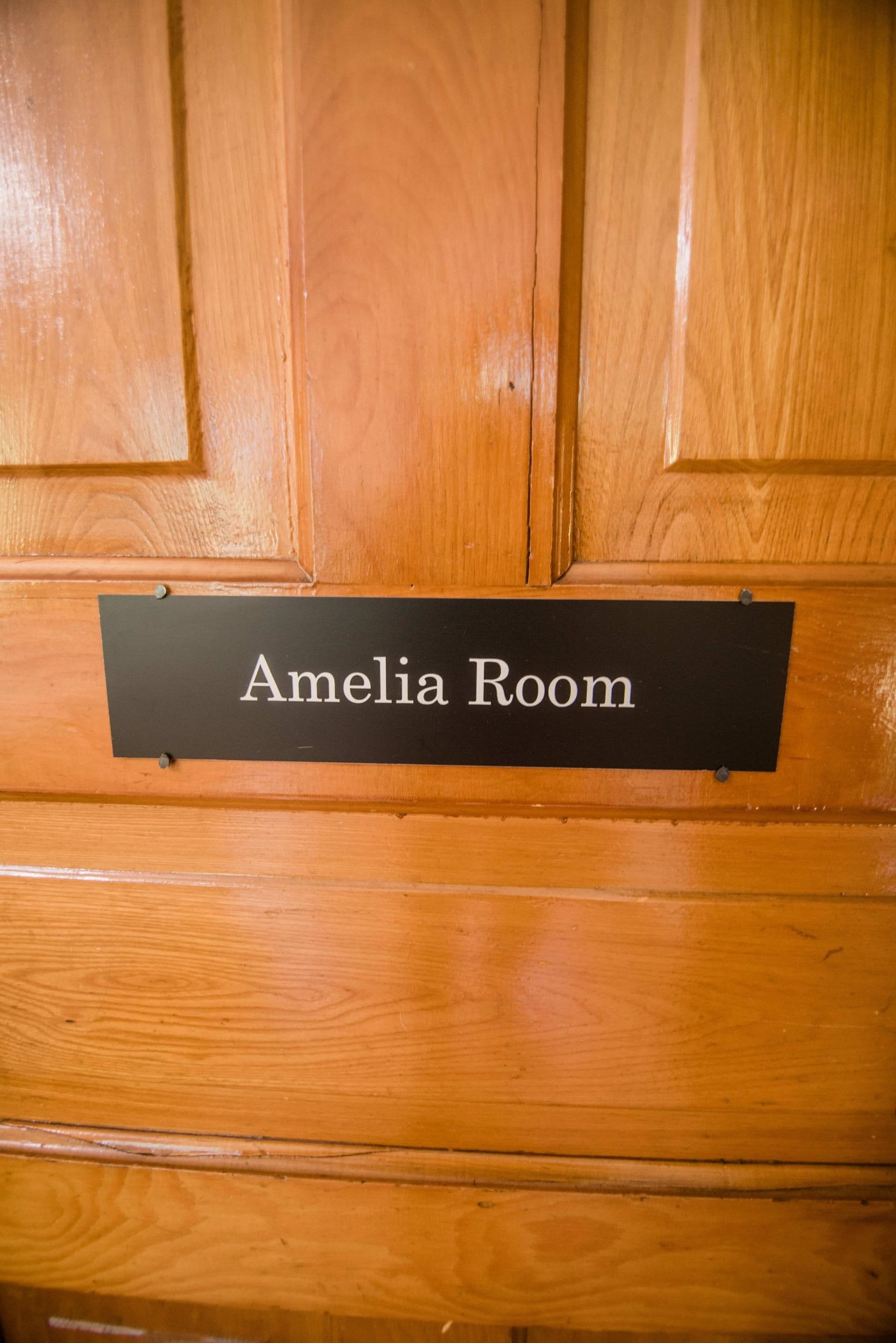 Una porta di legno con una targa che riporta la scritta 'Amelia Room'.