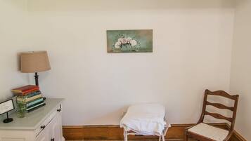 Un dormitorio con cama, mesita de noche con lámpara, una silla y un cuadro en la pared.