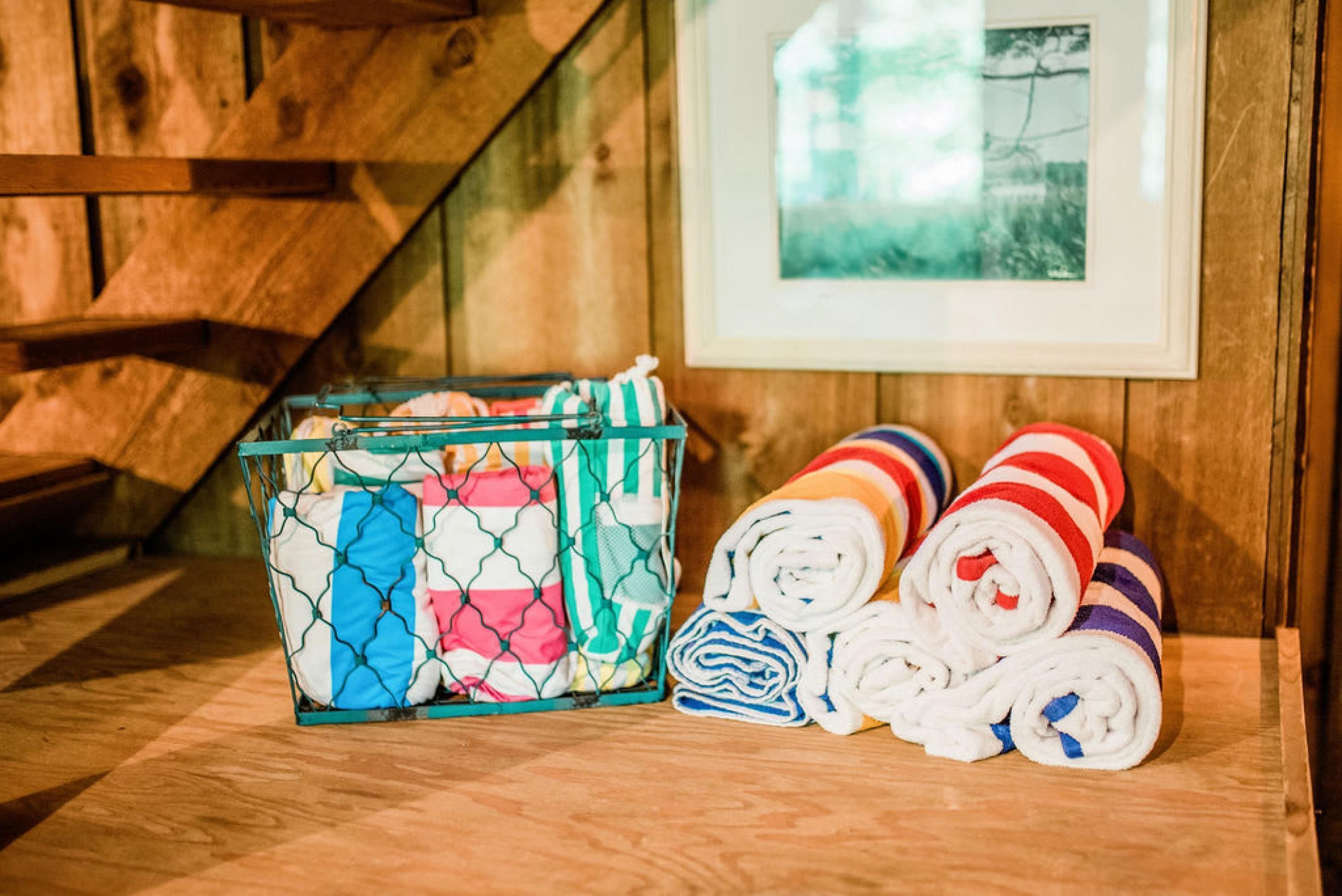 A wooden floor with a metal basket containing folded towels and a framed picture on the wall.