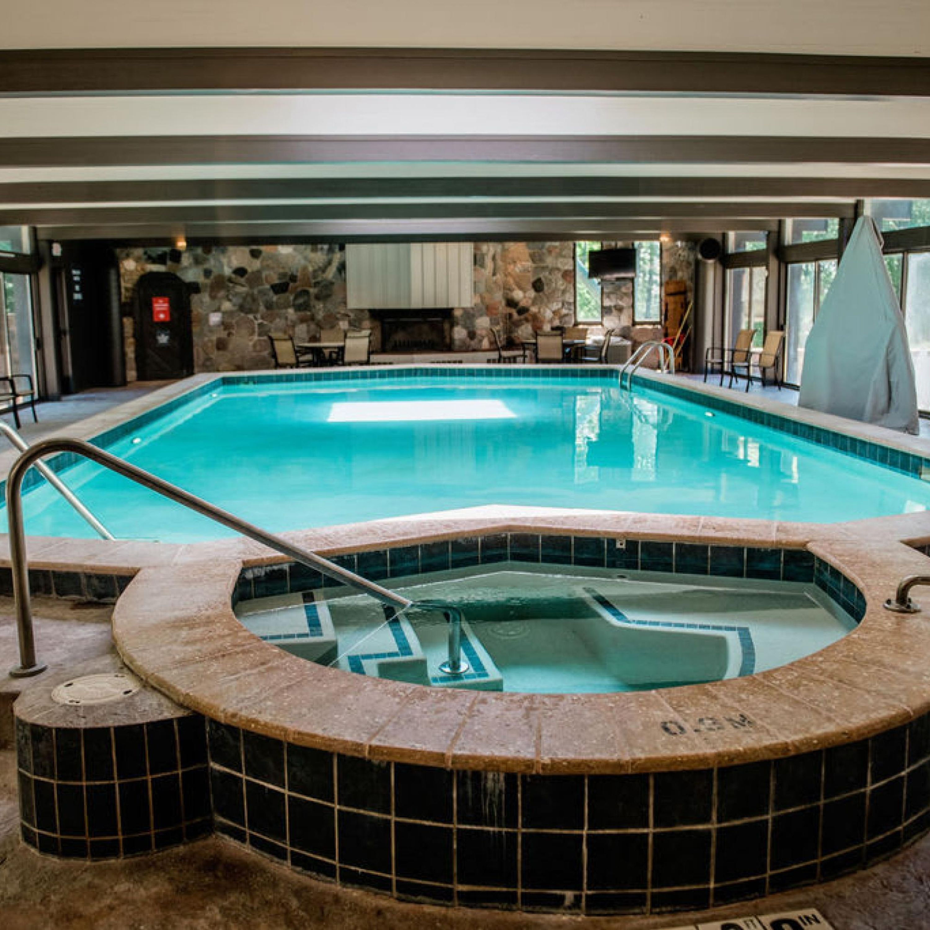 Een groot binnenzwembad met een jacuzzi, stenen muren en een open haard.