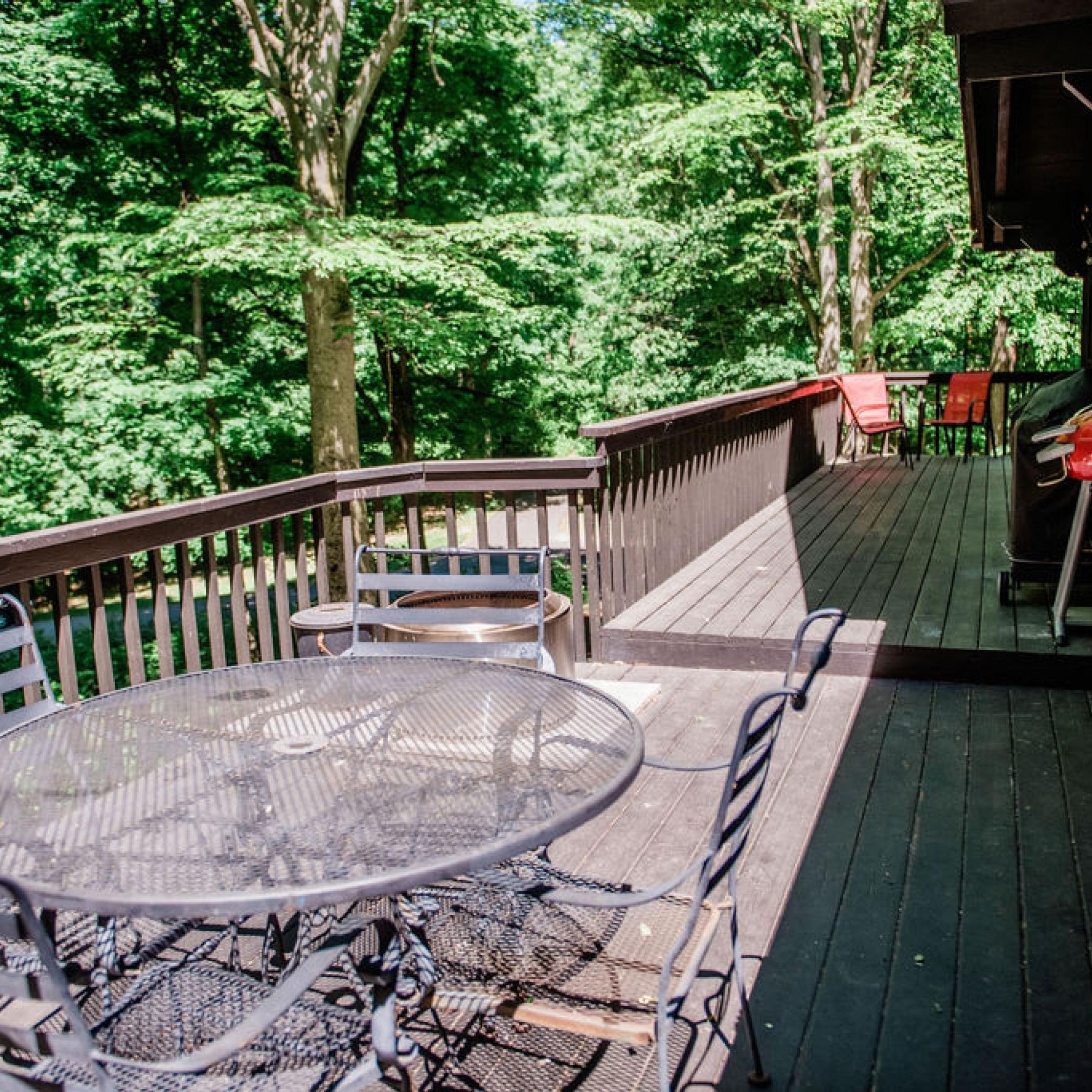 A deck with a round table and chairs, surrounded by a wooden railing, overlooking a forested area.