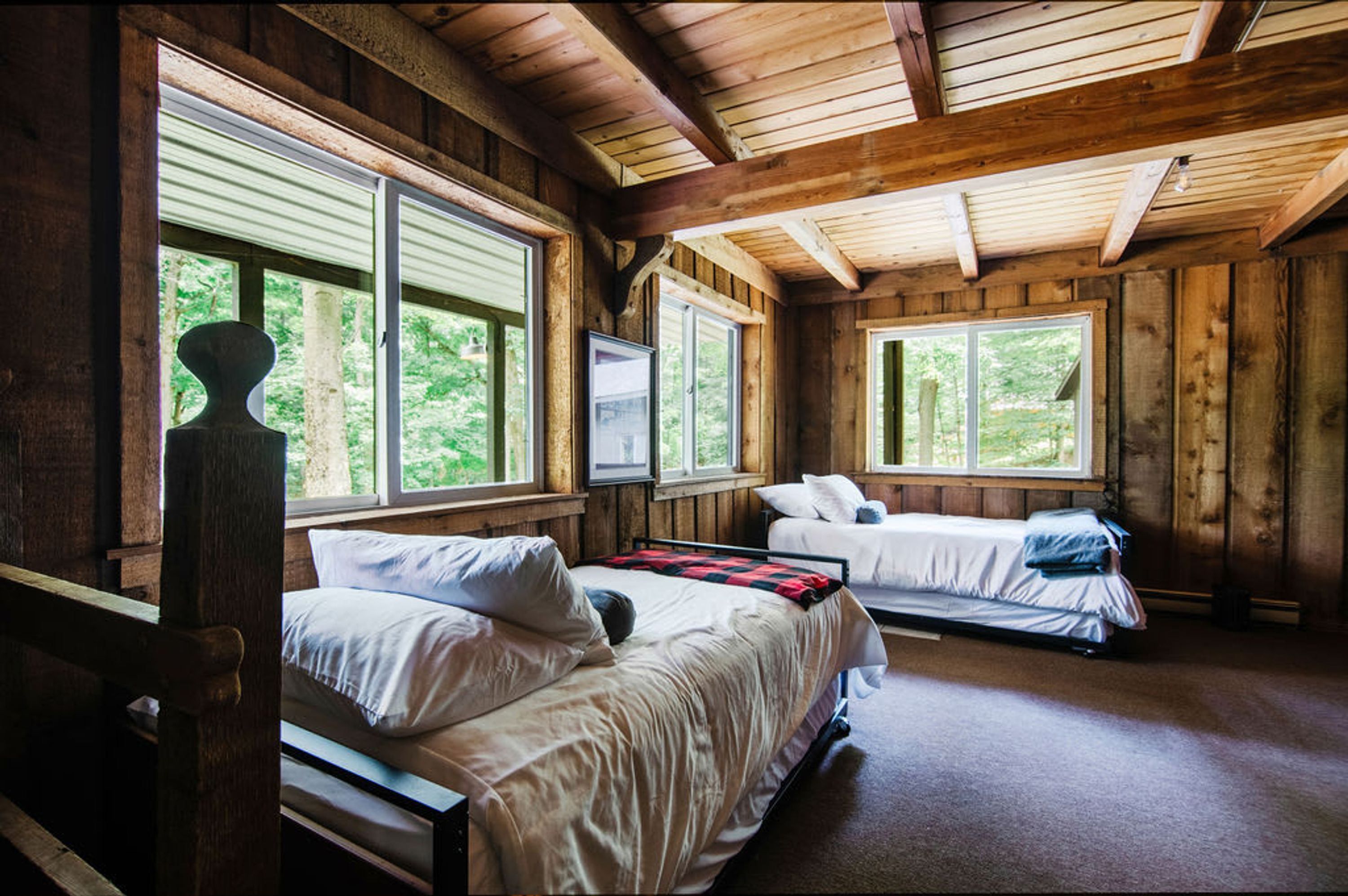 A cabin with two beds, wooden walls, and large windows.
