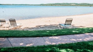 A beach with two lounge chairs facing the water, a clear sky, and a grassy area with a pathway. - Northern Nights Chalet by Wanderlust Abodes (Bellaire)