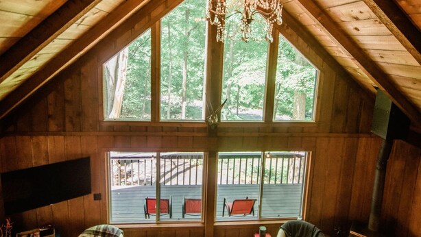 A cozy attic bedroom with wooden walls, a large window, and a chandelier. - Northern Nights Chalet by Wanderlust Abodes (Bellaire)