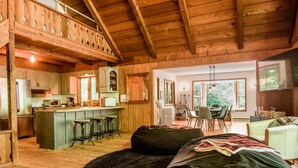 A spacious loft-style room with a high ceiling, wooden beams, a kitchen area, a dining area, and a cozy seating area with a large bean bag. - Northern Nights Chalet by Wanderlust Abodes (Bellaire)