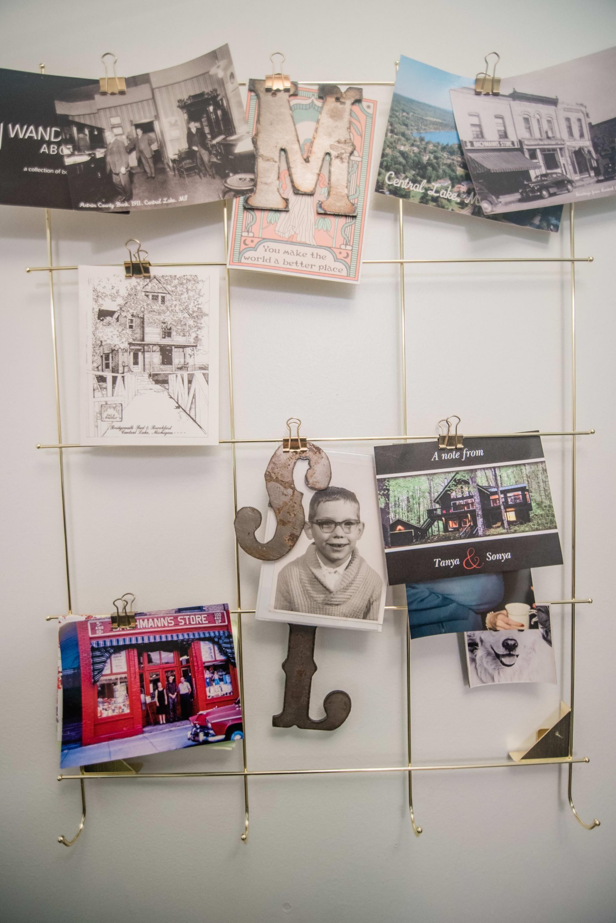 Eine Wand mit verschiedenen Fotografien und Erinnerungsstücken, darunter ein großes 'M', ein Schwarz-Weiß-Foto eines Gebäudes und ein Foto eines Geschäfts namens 'IMANN'S STORE'.