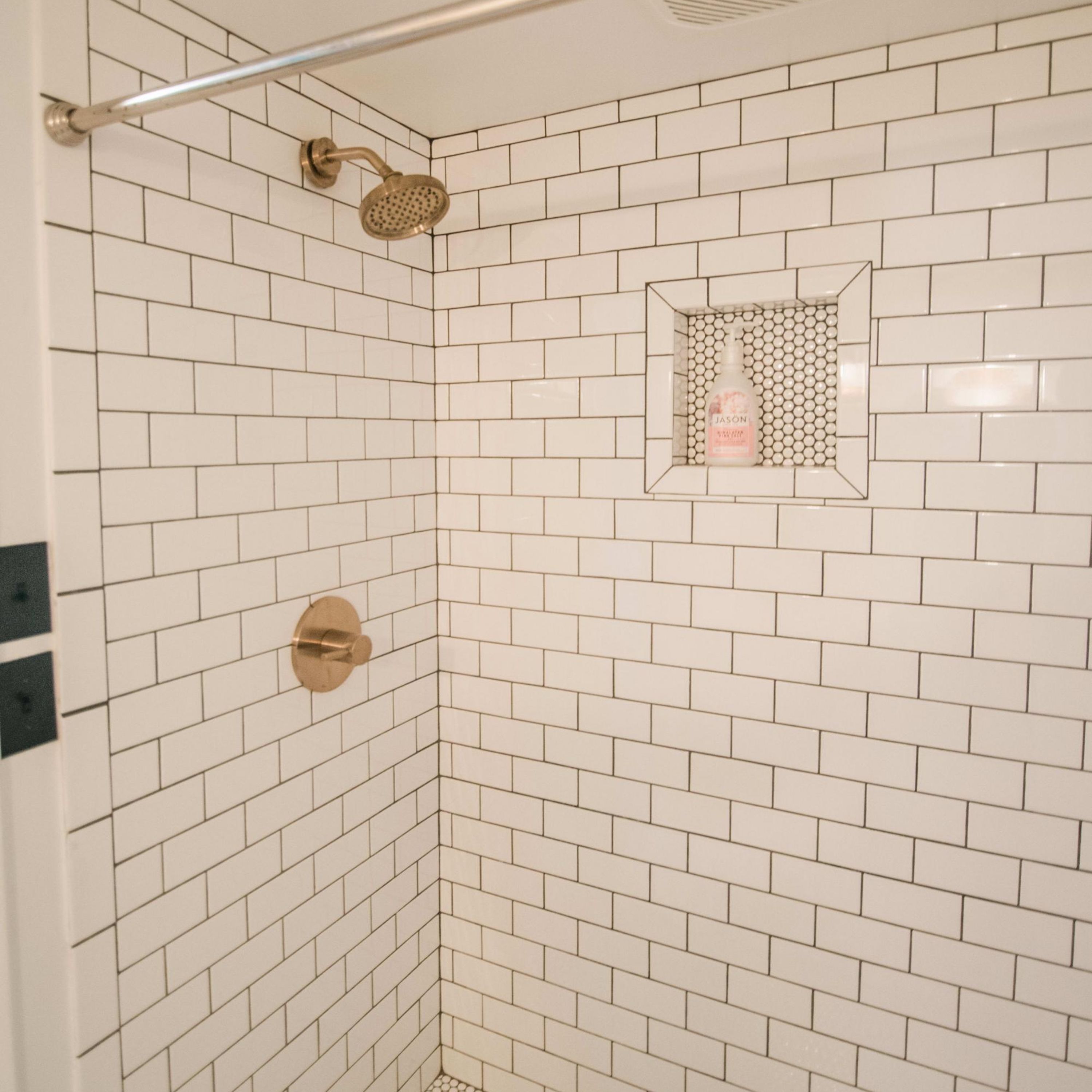A shower with white subway tiles, a handheld showerhead, and a soap dispenser in a corner.