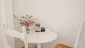 Ein weißer Esstisch mit zwei Korbstühlen, einer Blumenvase und einer kleinen Schale darauf.