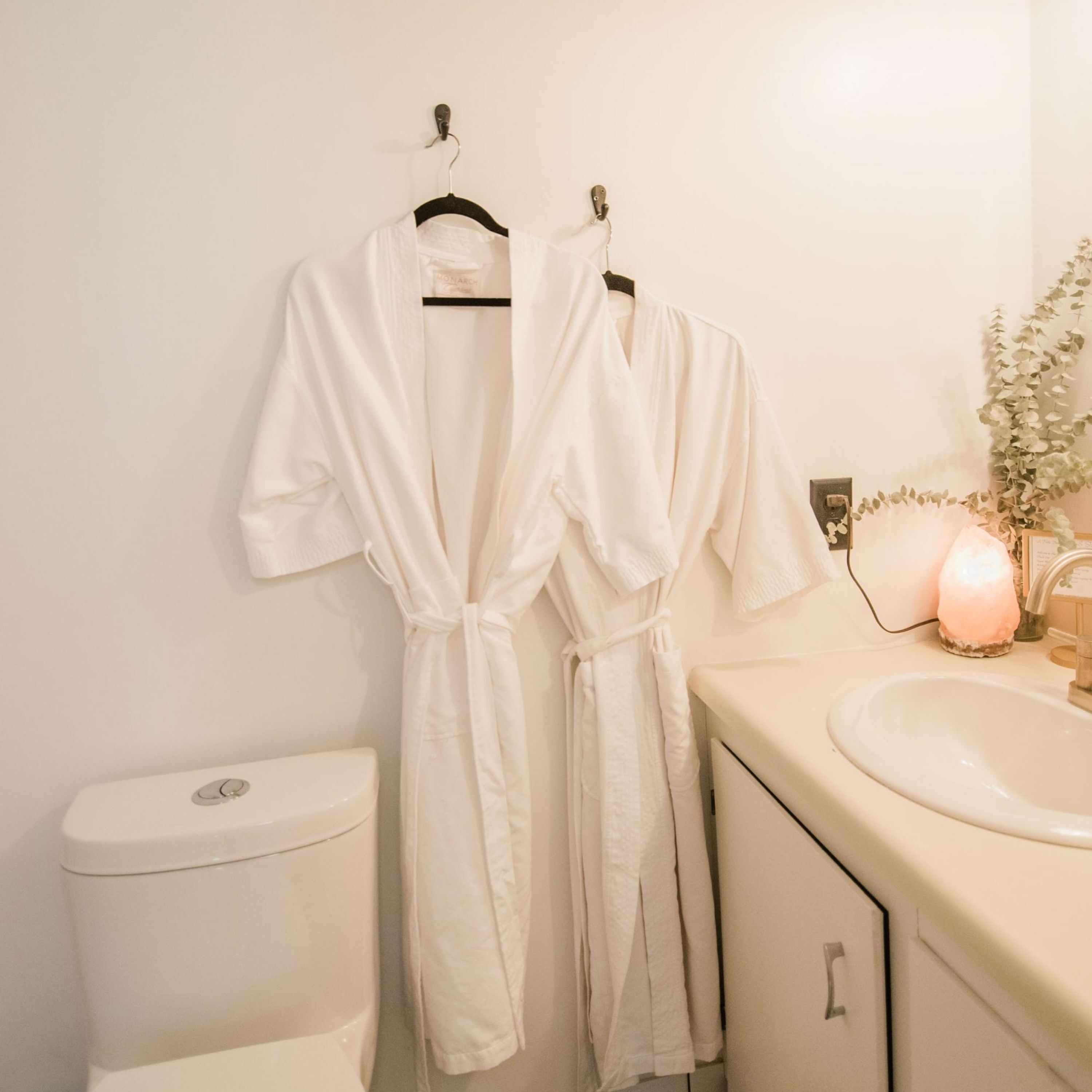 A bathroom with a toilet, sink, and two white robes hanging on a rack.