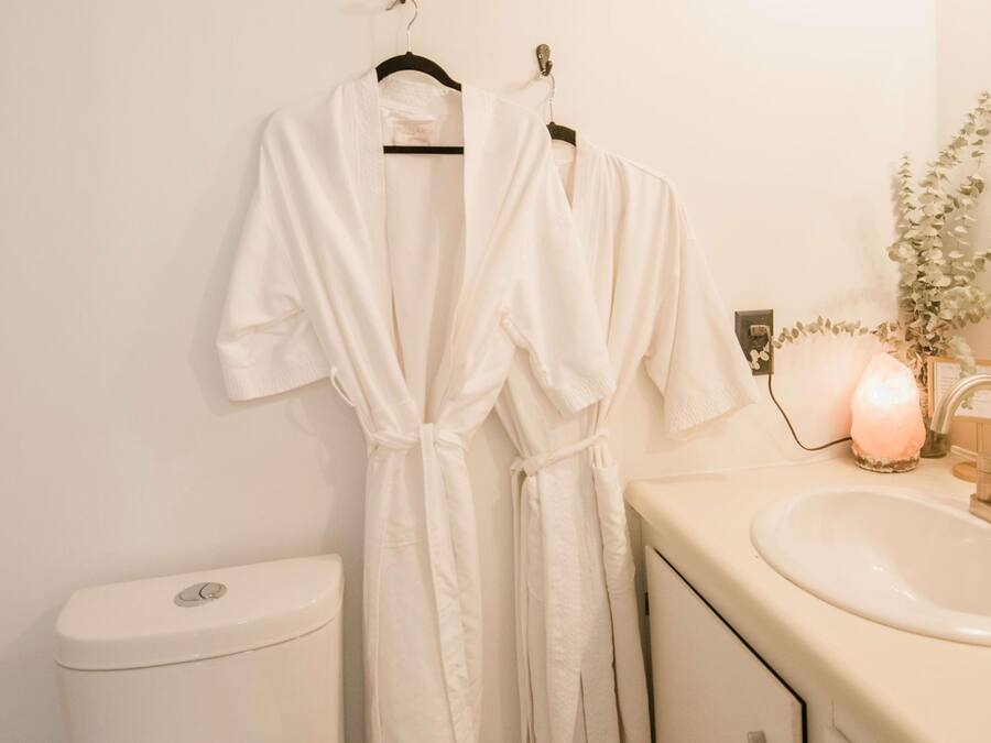 A bathroom with a toilet, sink, and two white robes hanging on a rack.