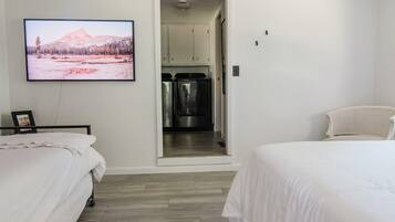 Un dormitorio con dos camas, un televisor en la pared y una kitchenette al fondo.