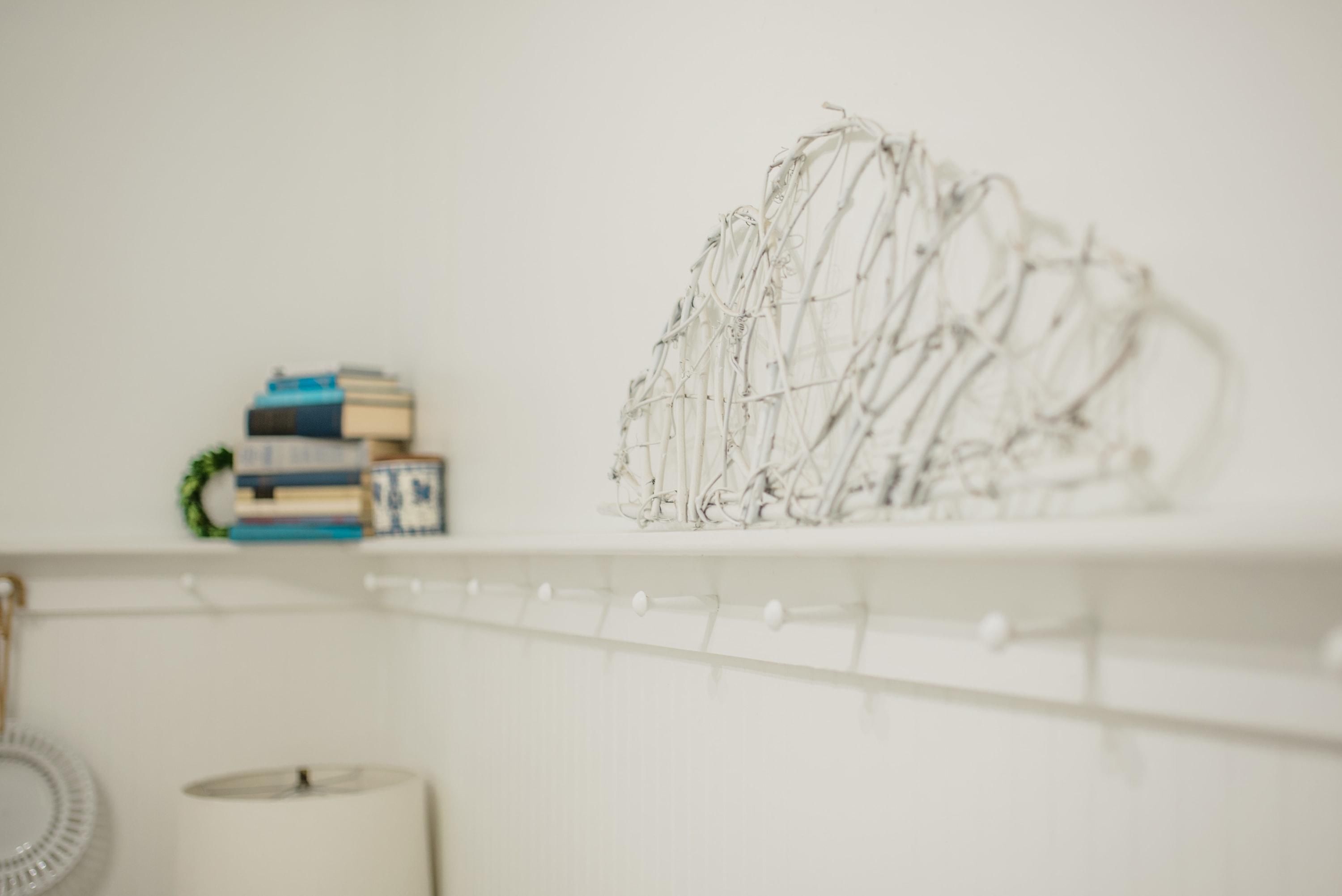 Une étagère blanche ornée d’une sculpture filaire décorative, une pile de livres et un mur blanc.