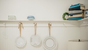 Une étagère blanche ornée d’assiettes décoratives, d’un bol et d’une pile de livres.