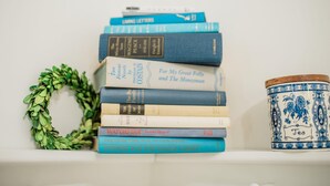Une pile de livres sur une étagère, avec une couronne décorative et un récipient en céramique.