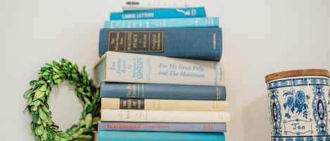 Een stapel boeken op een plank, met een decoratieve krans en een keramieken pot.