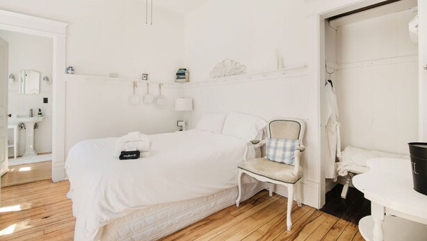 Une pièce blanche avec un lit, une chaise, une petite table, un lavabo et un ventilateur de plafond.