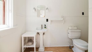 Une petite salle de bain blanche, avec un lavabo sur colonne, un miroir, des toilettes et une étagère au-dessus des toilettes.