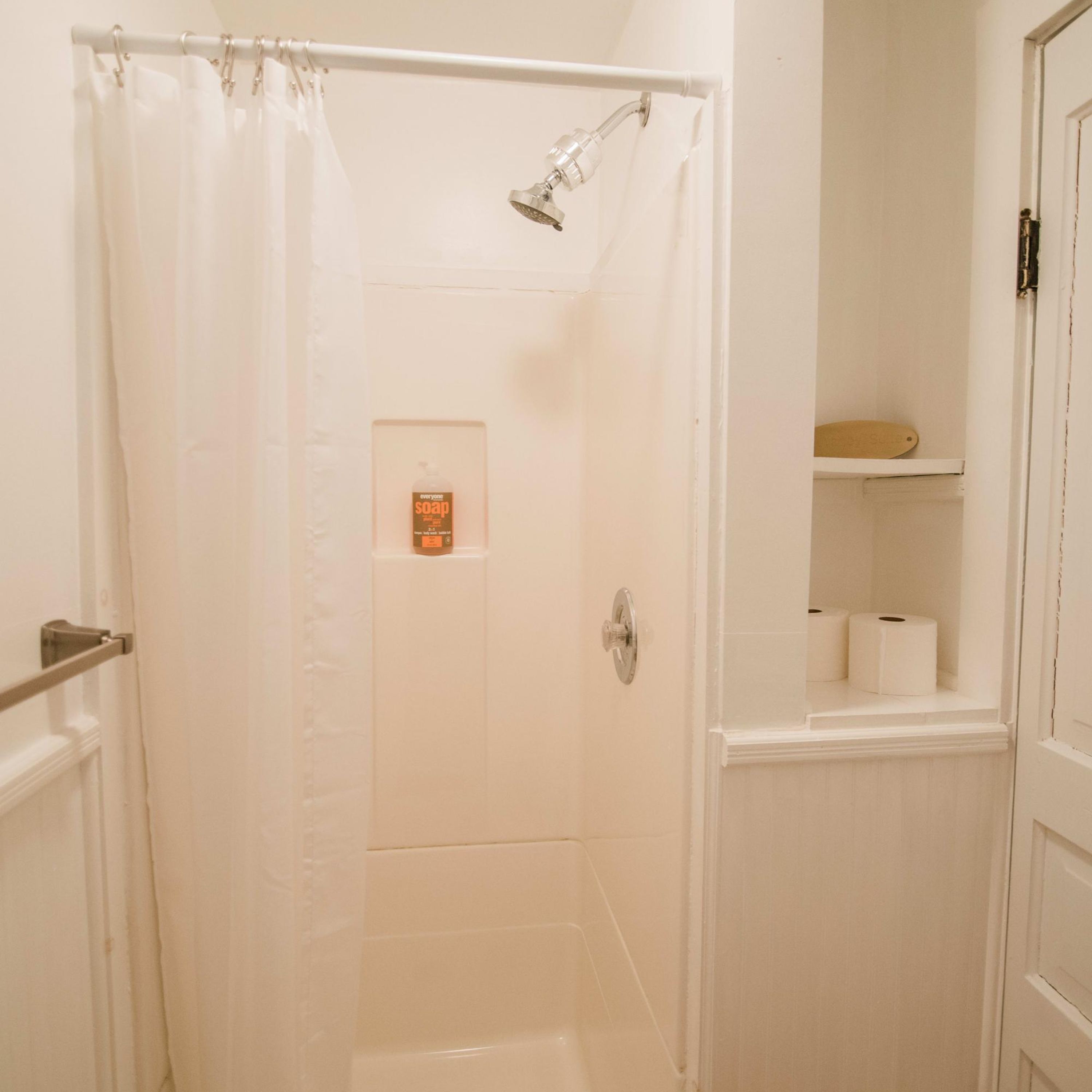 A bathroom with a shower curtain, a toilet paper holder, and a soap dispenser on the wall.