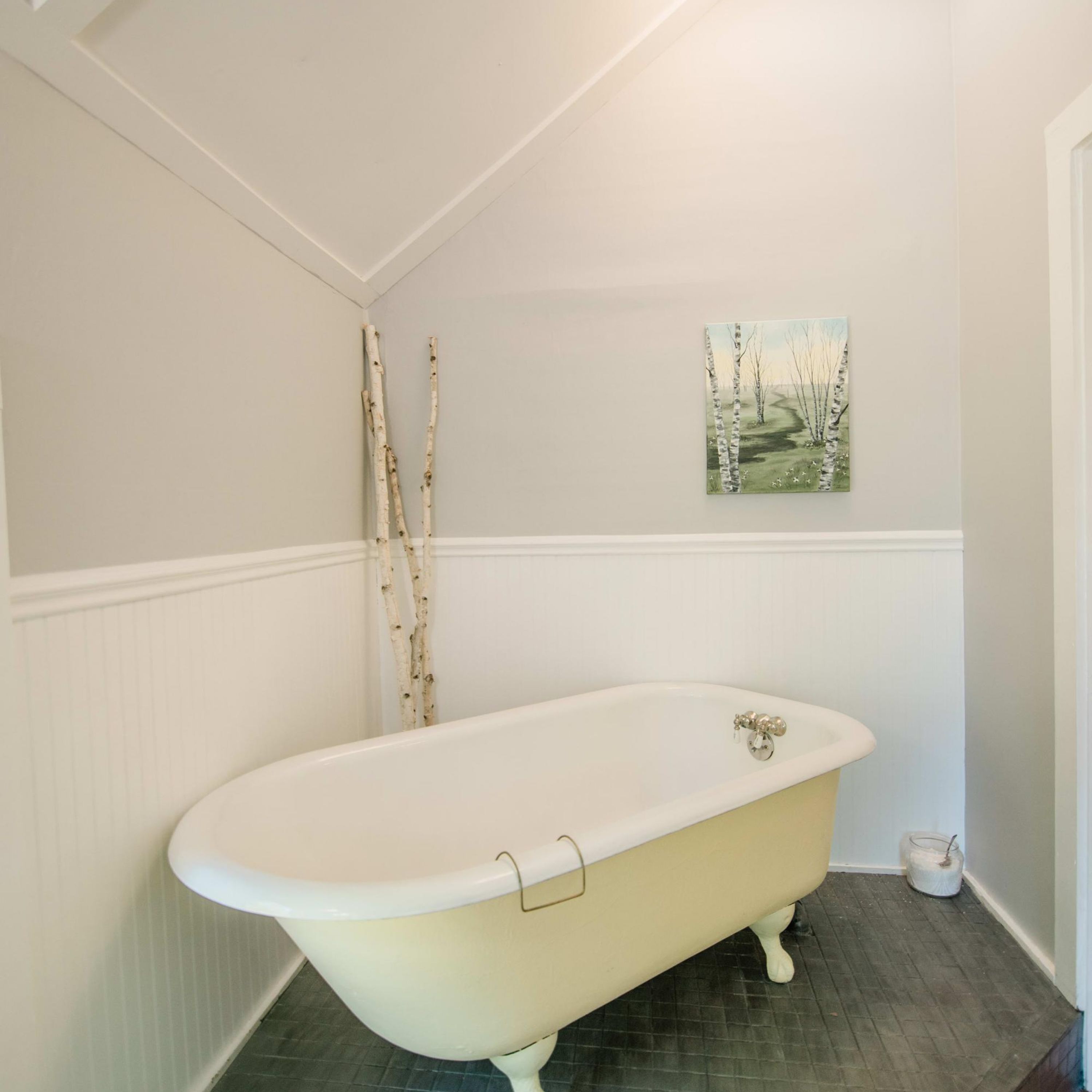 Un bagno con una vasca freestanding, un quadro raffigurante dei betuli e una porta bianca.