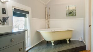 A bathroom with a clawfoot bathtub, a wooden floor, a window with a view, and a painting on the wall. - Mahaney Suite BW Boutique Hotel (Central Lake)