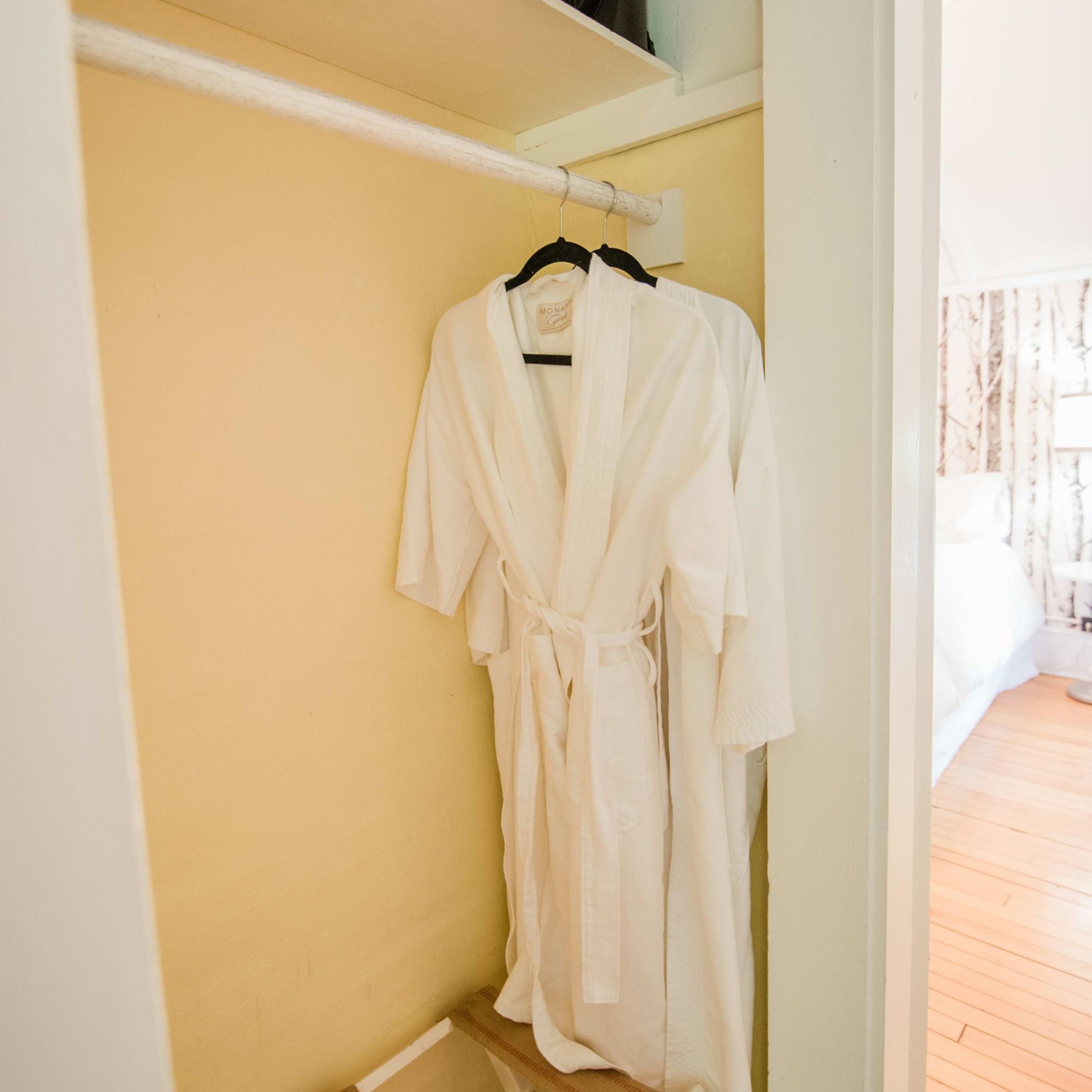 A white bathrobe hanging on a white towel rack in a room with a wooden floor and a yellow wall.
