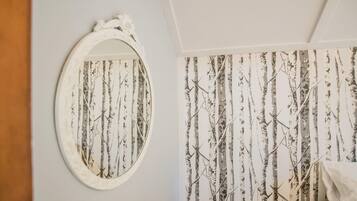 Una habitación con pared blanca, un espejo ovalado grande y un papel tapiz con diseño de árboles verticales.