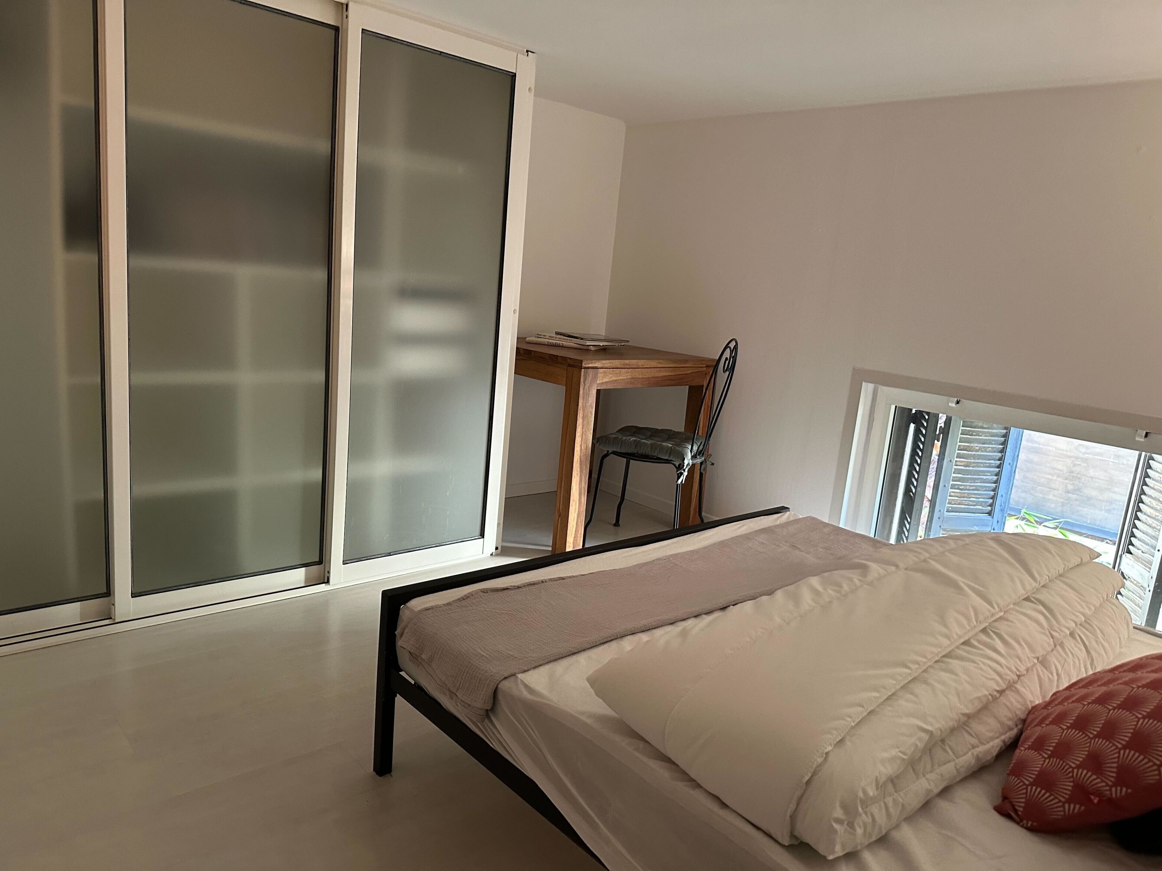 Une chambre à coucher comprenant un lit, une chaise, un bureau et une porte-fenêtre coulissante.